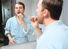 young man in bathrobe brushing teeth