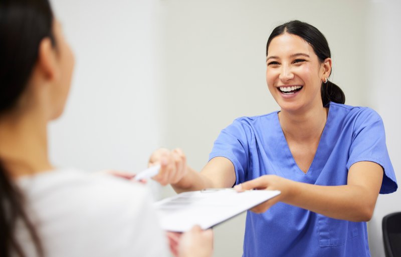 smiling team member handing over dental insurance forms 