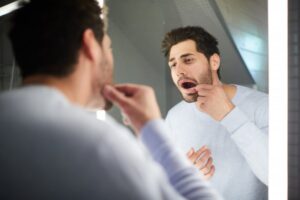 man looking at tooth in mirror 