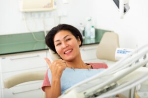 middle-aged woman giving thumbs up in dental chair 